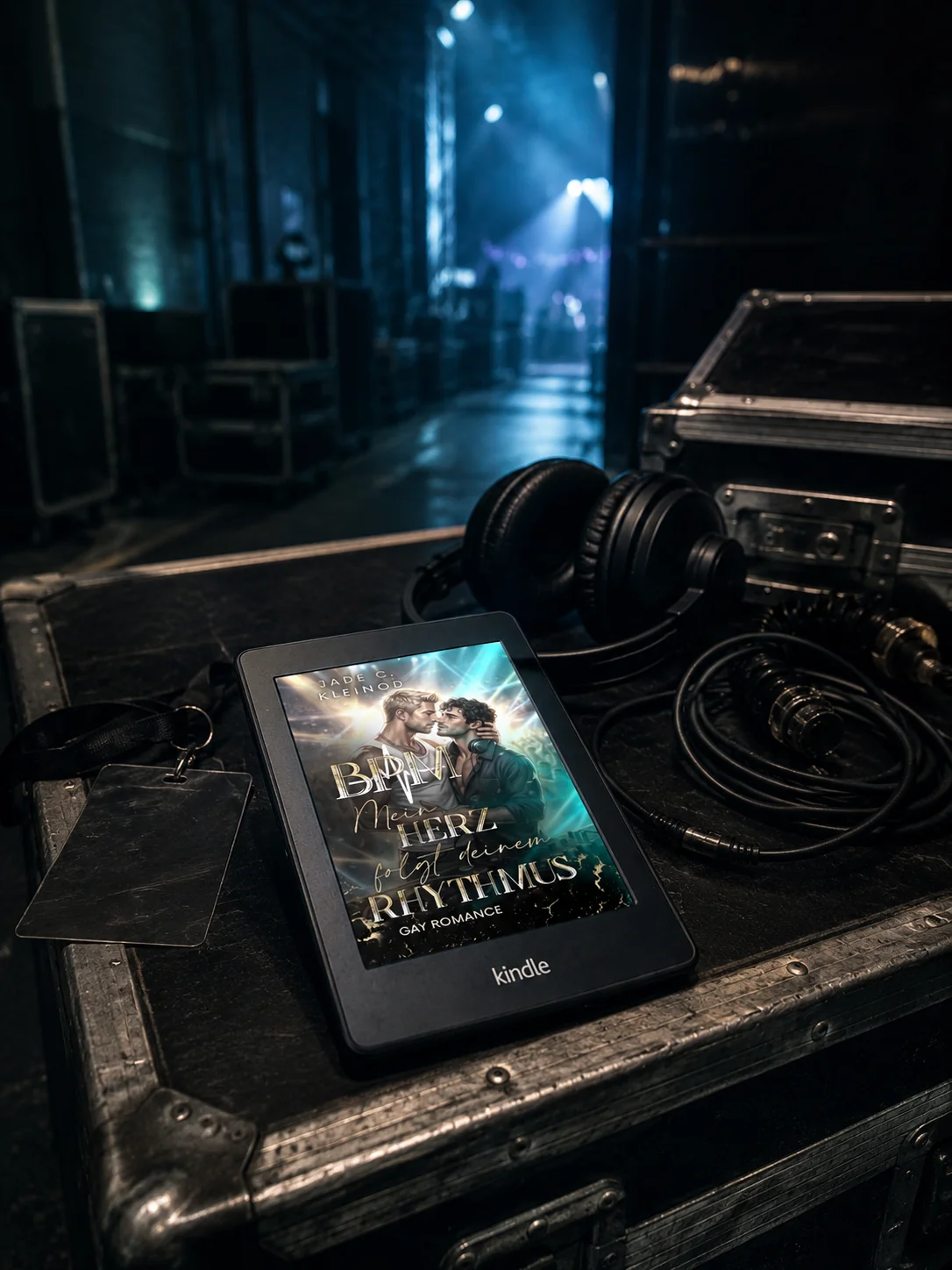 Kindle-Mockup des Covers von »BPM - Mein Herz folgt deinem Rhythmus«, platziert auf einem Flightcase backstage, im Hintergrund ein beleuchteter Bühnengang.